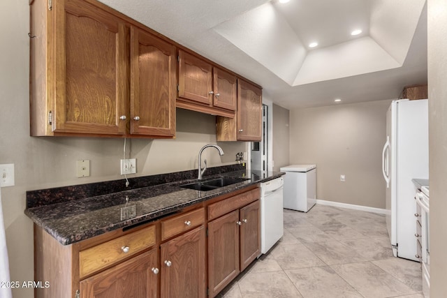 kitchen featuring light tile patterned floors, a raised ceiling, white appliances, dark stone countertops, and sink