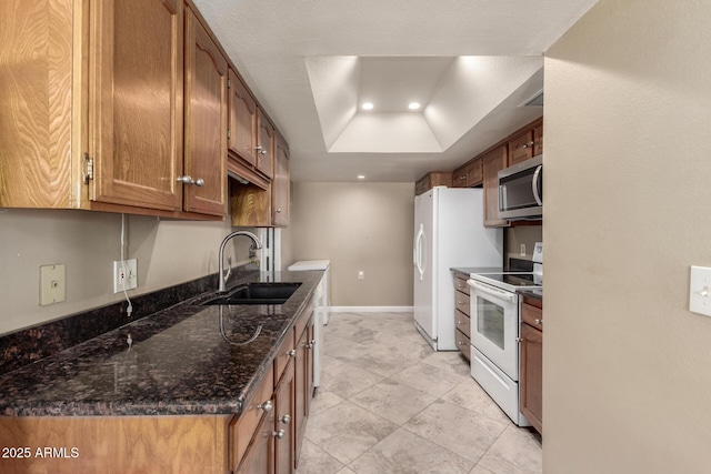 kitchen featuring dark stone counters, sink, a tray ceiling, and white appliances