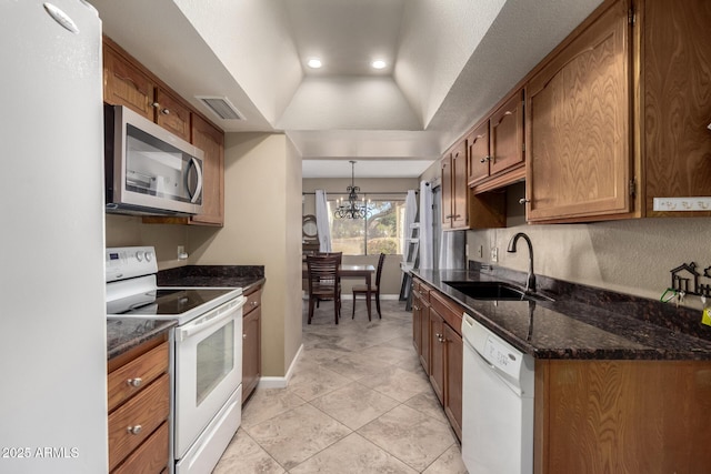 kitchen with a notable chandelier, a raised ceiling, sink, white appliances, and hanging light fixtures