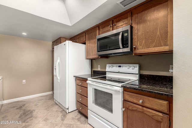 kitchen featuring white appliances, dark stone counters, and light tile patterned flooring