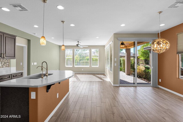 kitchen featuring sink, light hardwood / wood-style floors, decorative light fixtures, dark brown cabinets, and a center island with sink