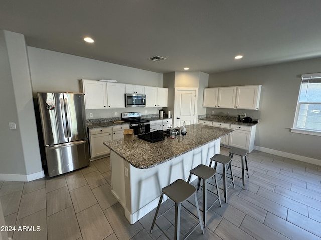 kitchen with appliances with stainless steel finishes, a center island with sink, dark stone countertops, white cabinets, and a breakfast bar area