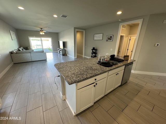 kitchen with stainless steel dishwasher, sink, a center island with sink, dark stone countertops, and white cabinets