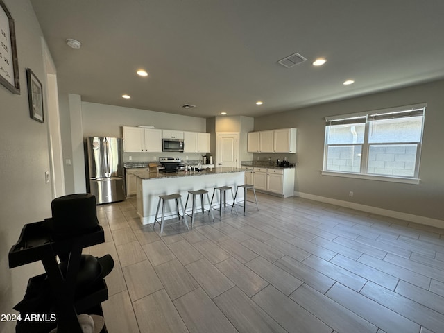 kitchen with a center island with sink, a kitchen breakfast bar, light wood-type flooring, appliances with stainless steel finishes, and white cabinetry