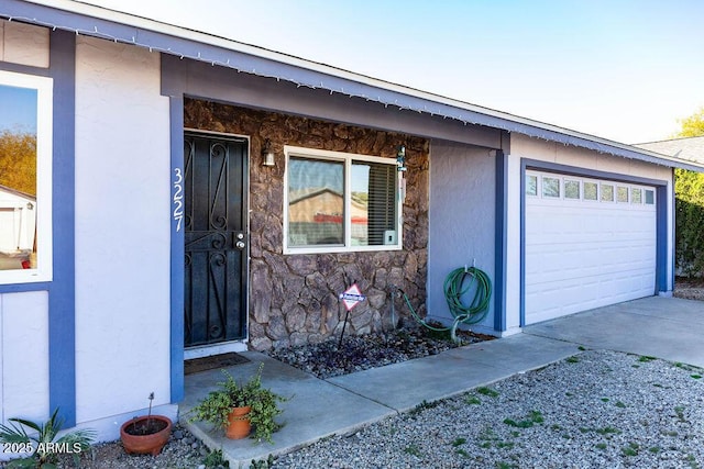 doorway to property featuring driveway, stone siding, an attached garage, and stucco siding