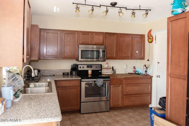 kitchen featuring brown cabinetry, stainless steel appliances, a sink, and light countertops