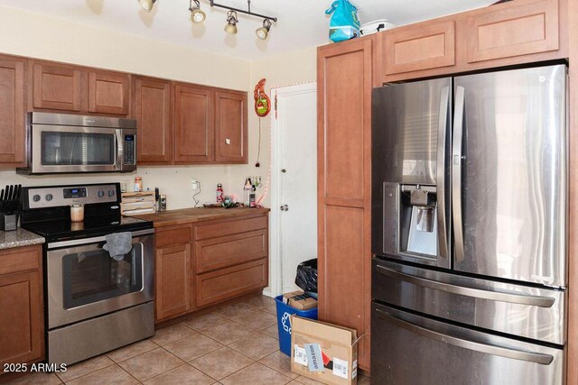 kitchen with brown cabinets, light tile patterned floors, and stainless steel appliances