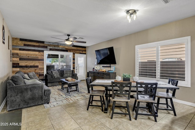 dining space featuring ceiling fan, wood walls, light tile patterned floors, and a textured ceiling