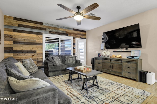 living room with ceiling fan, light tile patterned floors, and wooden walls