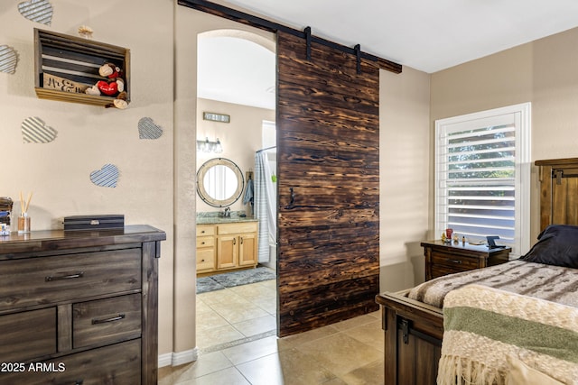 bedroom with a barn door, light tile patterned floors, and connected bathroom