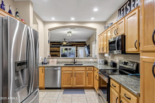 kitchen with ceiling fan, sink, dark stone counters, light tile patterned floors, and appliances with stainless steel finishes