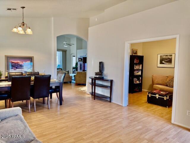 dining area with visible vents, ceiling fan with notable chandelier, arched walkways, light wood finished floors, and baseboards