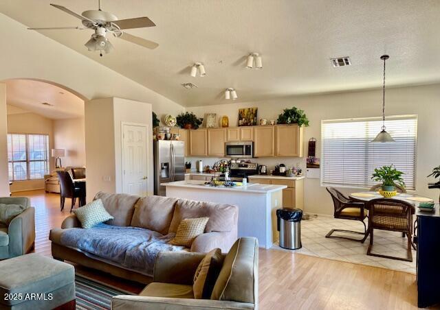 living area with visible vents, lofted ceiling, light wood-style flooring, arched walkways, and a ceiling fan