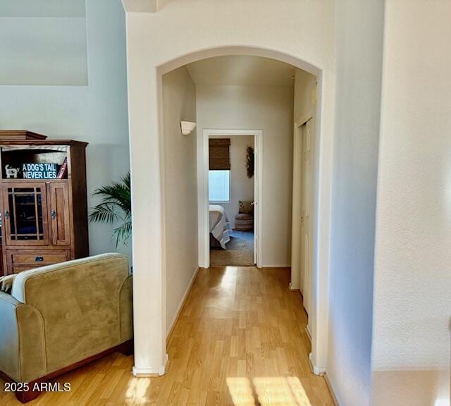 corridor featuring baseboards, arched walkways, and light wood-style floors