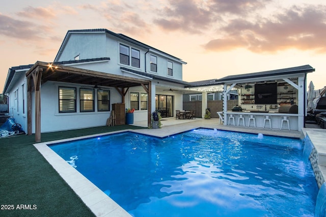 back house at dusk with a patio, exterior bar, and ceiling fan