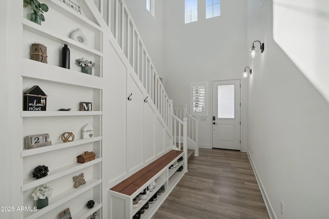 mudroom featuring built in shelves, wood-type flooring, and a towering ceiling