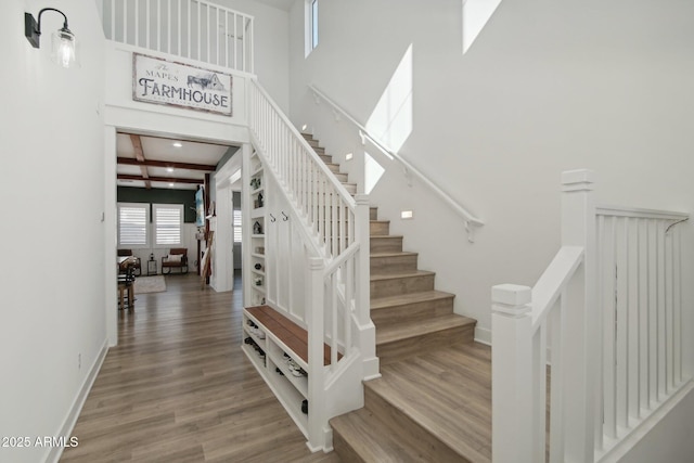 stairway featuring a towering ceiling, beam ceiling, and wood-type flooring