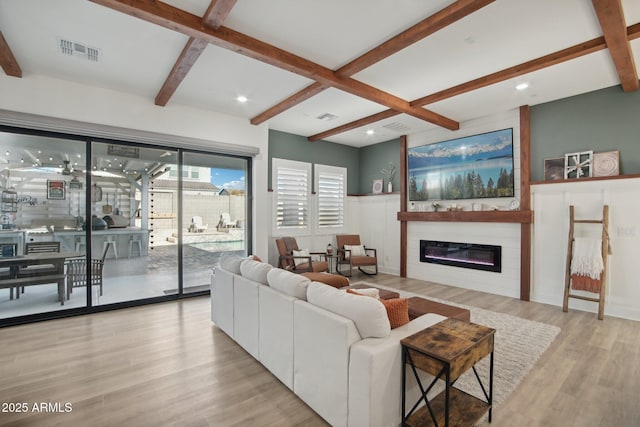 living room with a fireplace, beamed ceiling, and light wood-type flooring