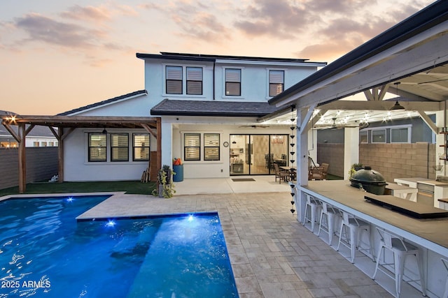 back house at dusk featuring a fenced in pool, a bar, and a patio