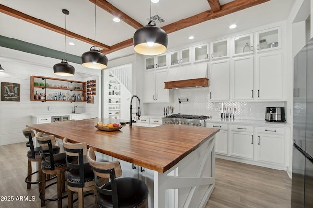 kitchen with white cabinetry, an island with sink, sink, hanging light fixtures, and beam ceiling