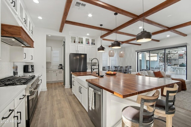 kitchen with wooden counters, white cabinetry, range with two ovens, an island with sink, and hanging light fixtures