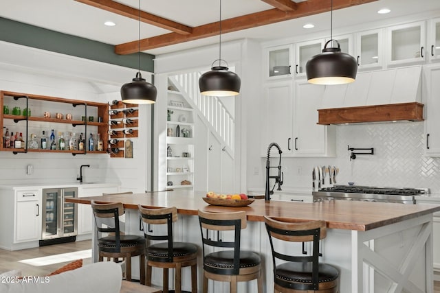 kitchen featuring white cabinets, beverage cooler, a center island with sink, and custom range hood