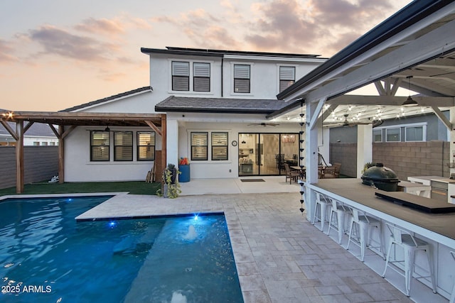 back house at dusk with a fenced in pool, a patio, a bar, and area for grilling