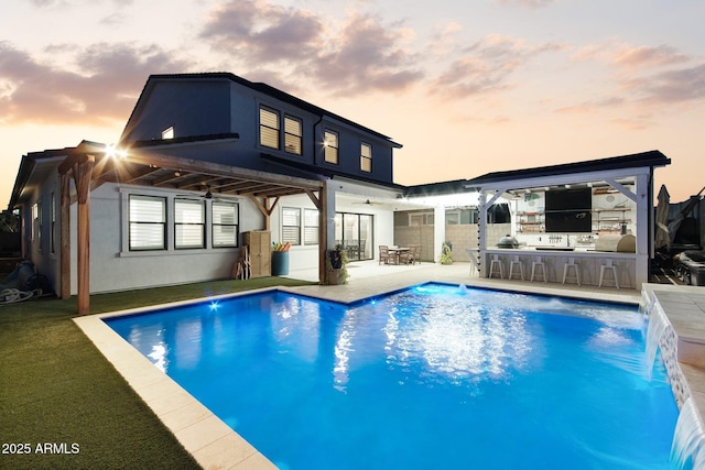 back house at dusk with pool water feature, a patio, an outdoor bar, and area for grilling