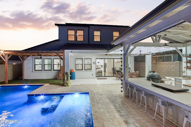 back house at dusk featuring exterior bar, an outdoor kitchen, pool water feature, and a patio