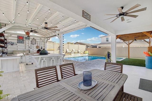 view of patio featuring exterior kitchen, an outdoor bar, a fenced in pool, and ceiling fan