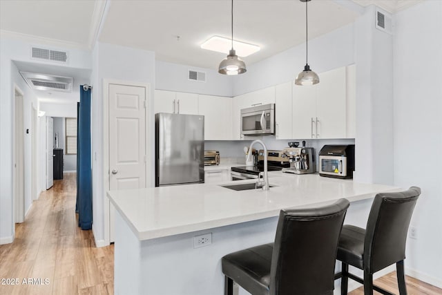 kitchen with white cabinetry, appliances with stainless steel finishes, kitchen peninsula, and hanging light fixtures