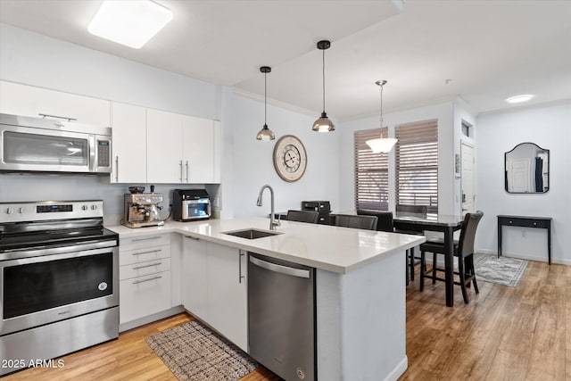 kitchen featuring appliances with stainless steel finishes, white cabinetry, sink, hanging light fixtures, and kitchen peninsula