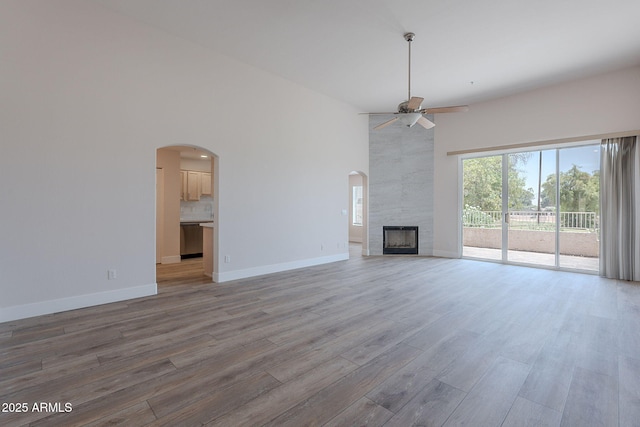 2647 N Miller Rd Unit 6, Scottsdale, AZ 85257 - unfurnished living room featuring a ceiling fan, wood finished floors, a towering ceiling, a tile fireplace, and arched walkways