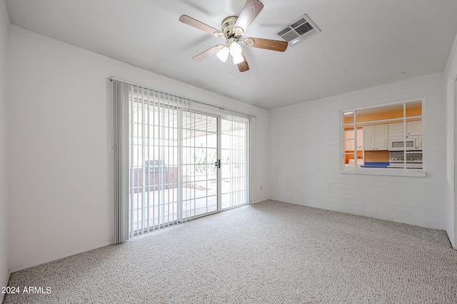 unfurnished room with carpet flooring, ceiling fan, and brick wall