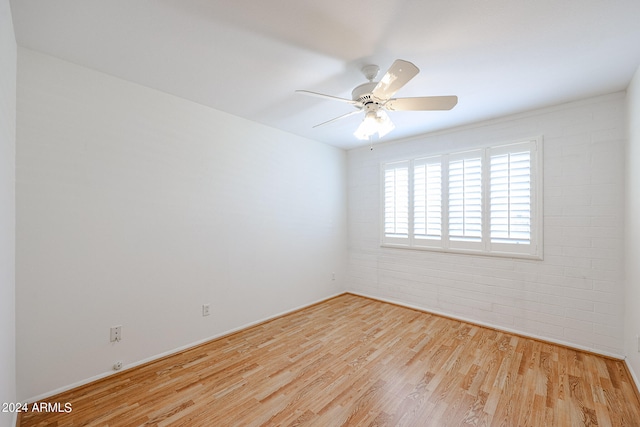 empty room featuring light hardwood / wood-style flooring, brick wall, and ceiling fan