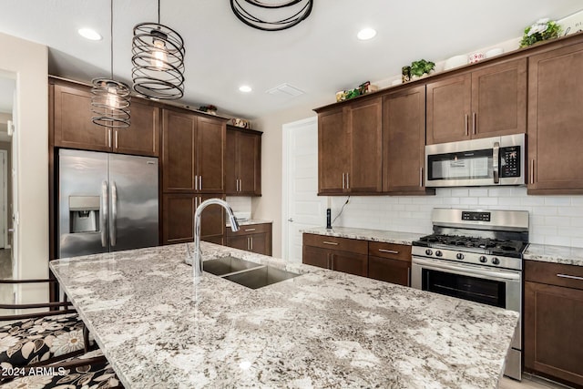 kitchen with dark brown cabinetry, sink, light stone counters, decorative light fixtures, and appliances with stainless steel finishes