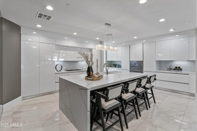 kitchen with backsplash, white cabinetry, a large island, and hanging light fixtures