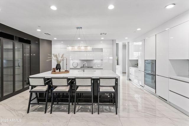 kitchen featuring white cabinetry, hanging light fixtures, and an island with sink