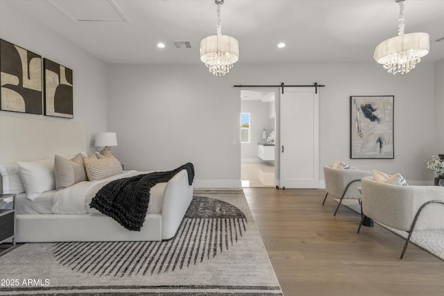 bedroom with hardwood / wood-style flooring, ensuite bath, a barn door, and an inviting chandelier