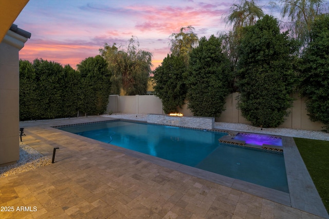 pool at dusk with a patio area and an in ground hot tub