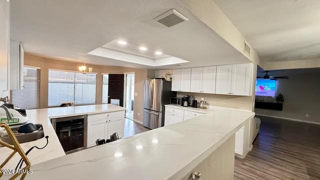 kitchen featuring stainless steel fridge, a tray ceiling, light stone counters, white cabinetry, and beverage cooler