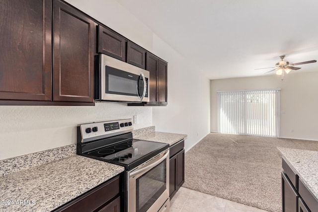 kitchen with appliances with stainless steel finishes, ceiling fan, dark brown cabinetry, light stone countertops, and light colored carpet