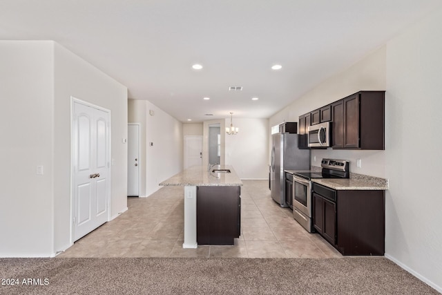 kitchen with light stone counters, stainless steel appliances, a center island with sink, light tile patterned floors, and an inviting chandelier