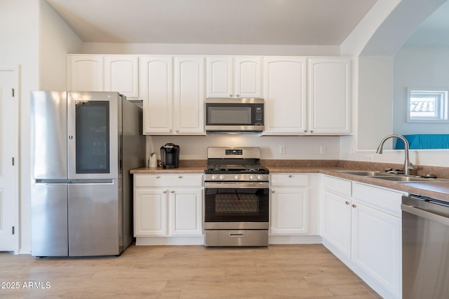 1956 N Hubbard Ln, Casa Grande, AZ 85122 - kitchen featuring white cabinetry, arched walkways, a sink, light wood-style flooring, and stainless steel appliances