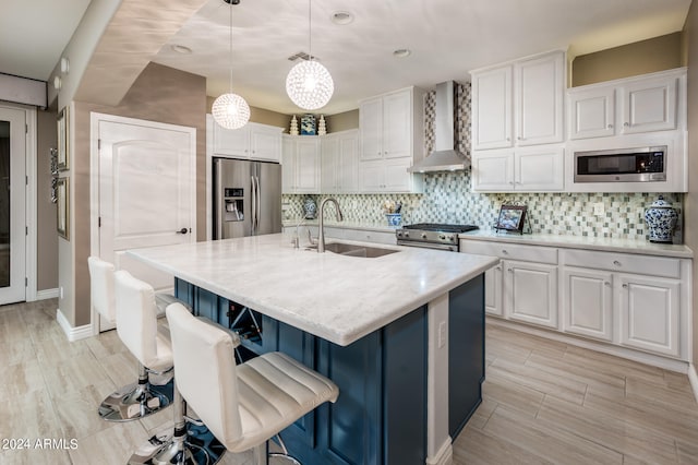 kitchen featuring wall chimney exhaust hood, a center island with sink, sink, white cabinetry, and appliances with stainless steel finishes