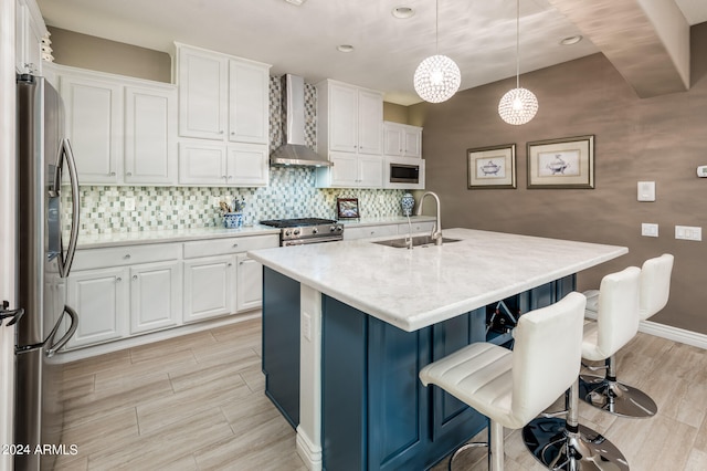 kitchen with wall chimney range hood, hanging light fixtures, sink, white cabinetry, and appliances with stainless steel finishes