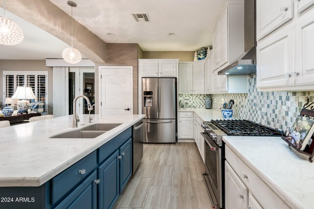 kitchen featuring wall chimney exhaust hood, stainless steel appliances, sink, pendant lighting, and blue cabinets