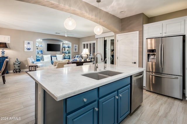 kitchen featuring appliances with stainless steel finishes, sink, blue cabinets, decorative light fixtures, and a center island with sink