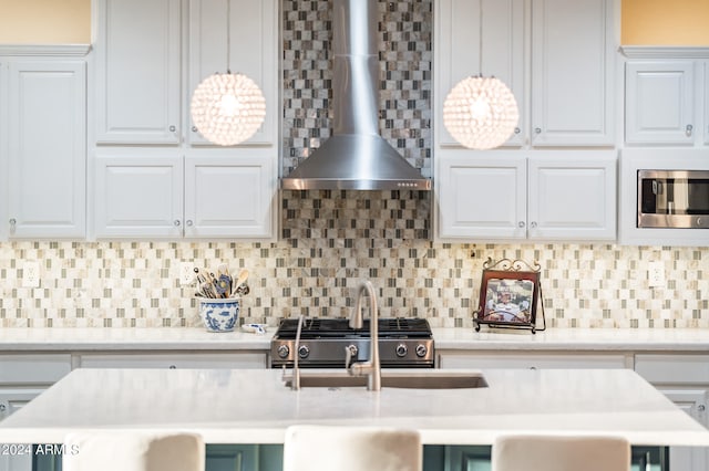 kitchen featuring wall chimney range hood, decorative backsplash, hanging light fixtures, white cabinetry, and stainless steel appliances