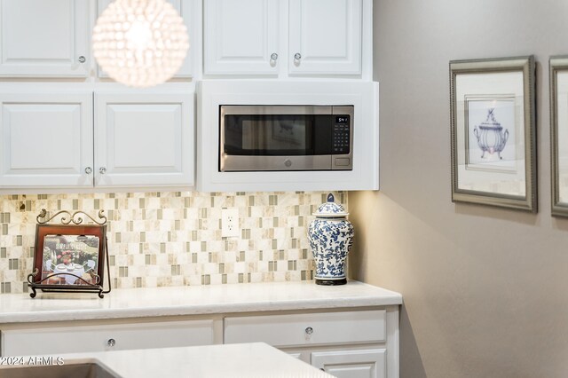 kitchen featuring white cabinets, stainless steel microwave, and backsplash